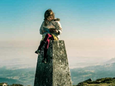 A girl reads a book on top of a pedestal on a mountain.