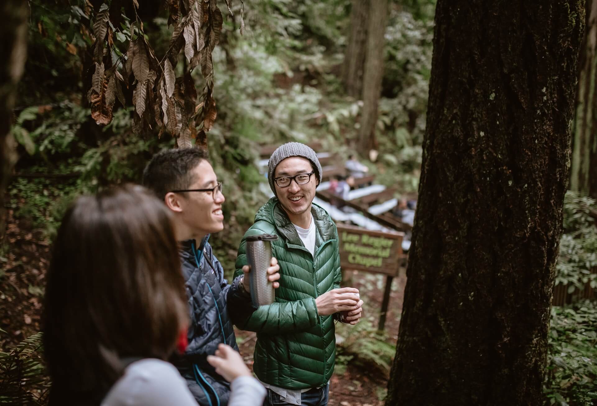 Three people in outdoor apparel laugh in a forest.