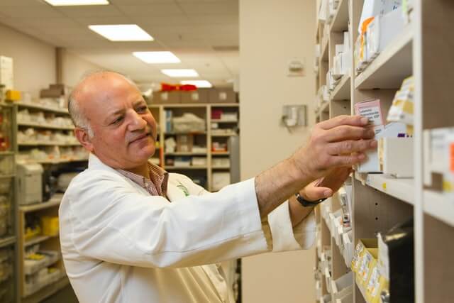 A pharmacist in a white coat examines medicine on a shelf.