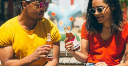 A man and woman sit in the sun with cold beverages.