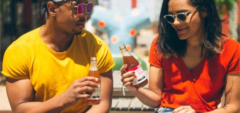 A man and woman sit in the sun with cold beverages.