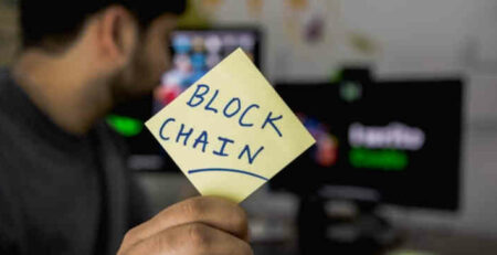 Someone holds a sticky note that says “blockchain” on it.