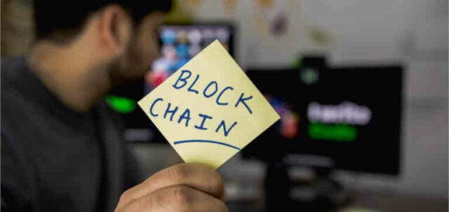 Someone holds a sticky note that says “blockchain” on it.
