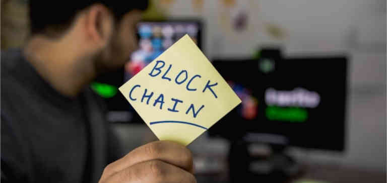 Someone holds a sticky note that says “blockchain” on it.