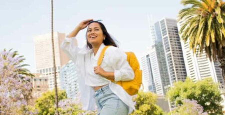 A woman wearing sunglasses and a yellow backpack walks outside.