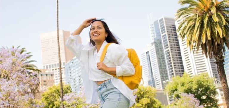 A woman wearing sunglasses and a yellow backpack walks outside.