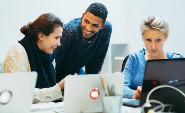 A man smiles while two women work on laptop computers.