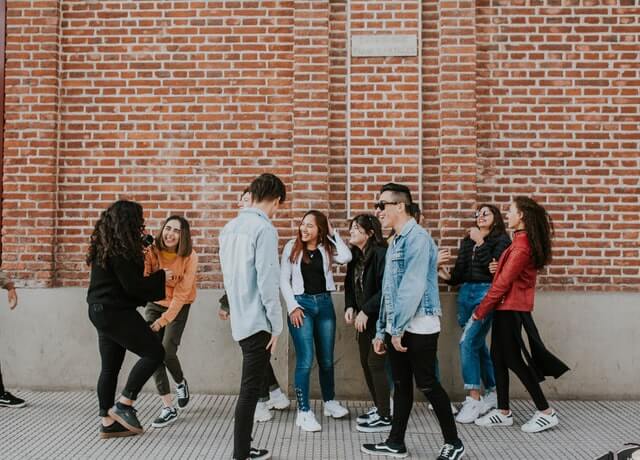 Many people stand near a brick wall laughing with one another.