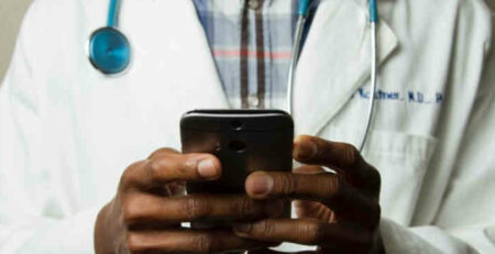 A doctor in a medical coat holds a cell phone.