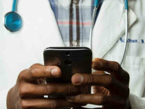 A doctor in a medical coat holds a cell phone.