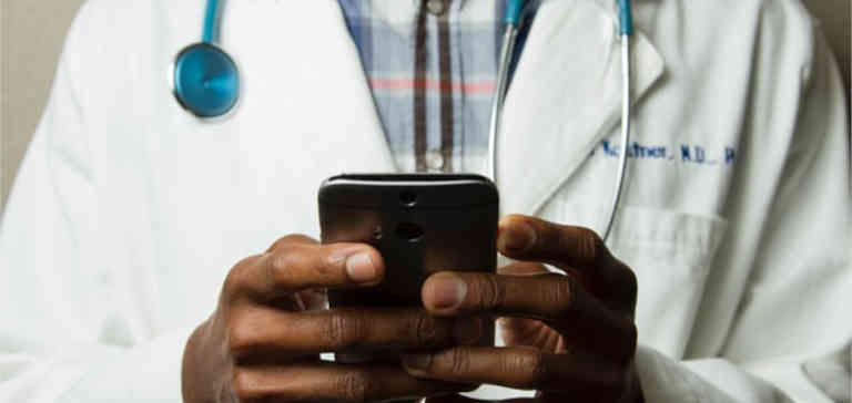 A doctor in a medical coat holds a cell phone.