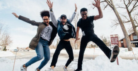 Three people jump in the air in a snowy field.