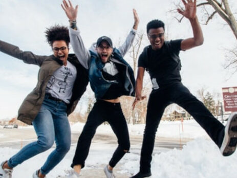 Three people jump in the air in a snowy field.