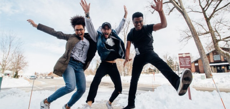 Three people jump in the air in a snowy field.