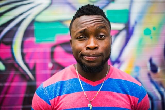 A man in a colorful shirt standing in front of wall graffiti.