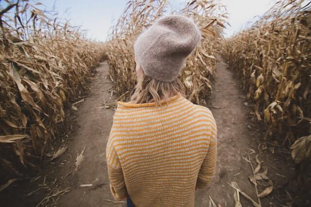 A woman in a yellow sweater and hat stands near two roads.