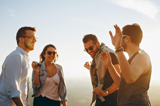 A group of people stands outside laughing in the sunshine.