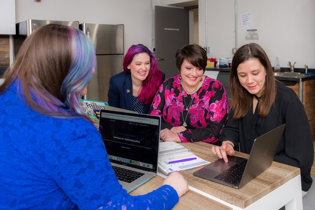A group of women meets around a laptop.