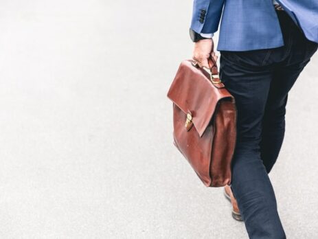 Someone in a blue suit jacket holding a suitcase.