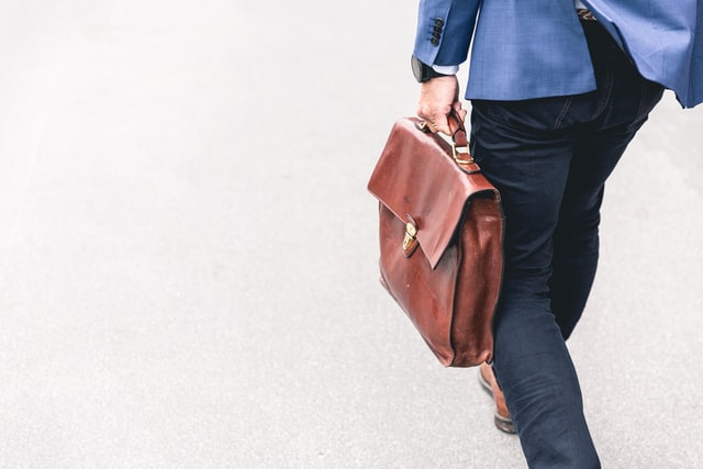 Someone in a blue suit jacket holding a suitcase.