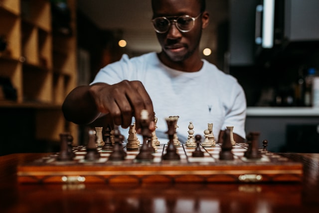 A man wearing glasses plays chess at a chessboard.