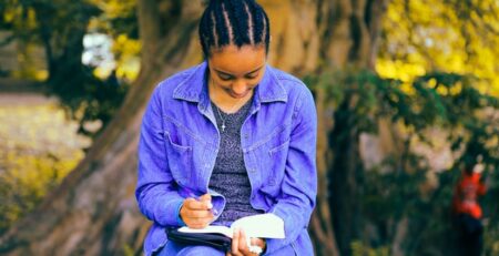 A person reading a book while sitting underneath a tree.