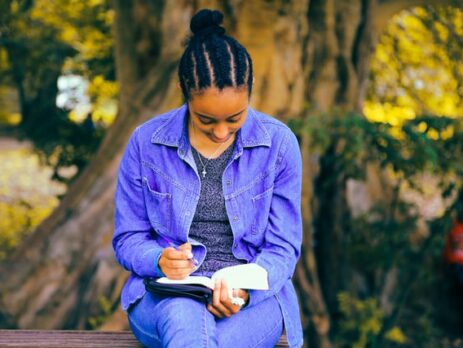 A person reading a book while sitting underneath a tree.