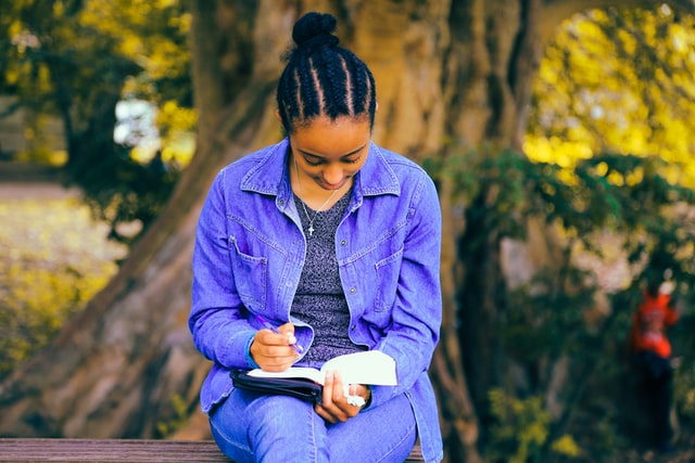 A person reading a book while sitting underneath a tree.