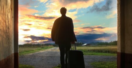 A man with a suitcase walking through a doorway outside.