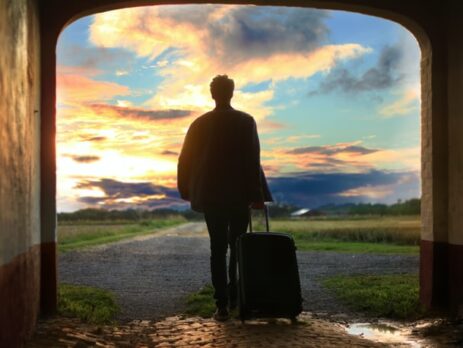 A man with a suitcase walking through a doorway outside.