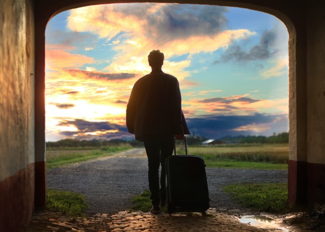 A man with a suitcase walking through a doorway outside.