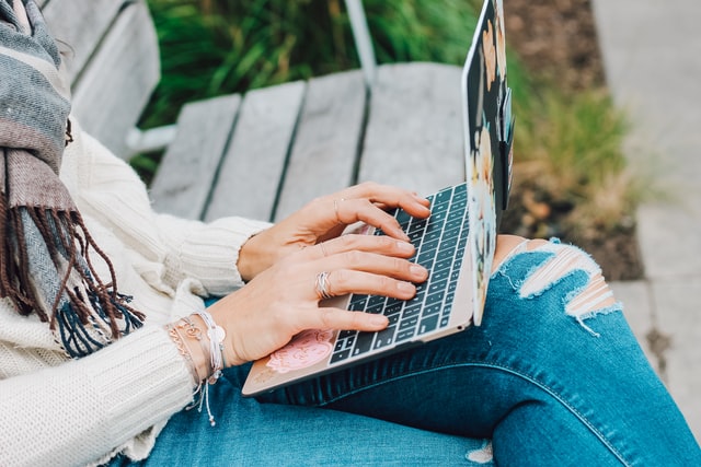 A person sitting on a bench typing on a small laptop.