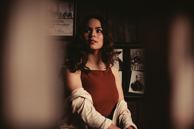 A woman with dark curly hair and a white shirt looks away from the camera.