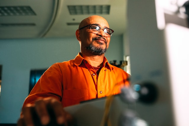 A man wearing glasses smiles while he works on a laptop.