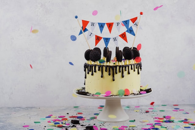 A white birthday cake on a plate with a banner and other decorations.