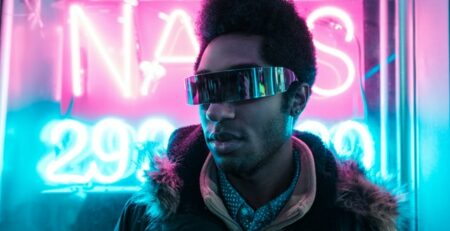 A man wearing futuristic sunglasses in front of neon lights.