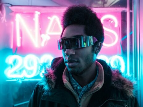 A man wearing futuristic sunglasses in front of neon lights.