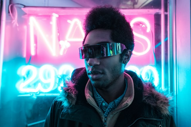 A man wearing futuristic sunglasses in front of neon lights.