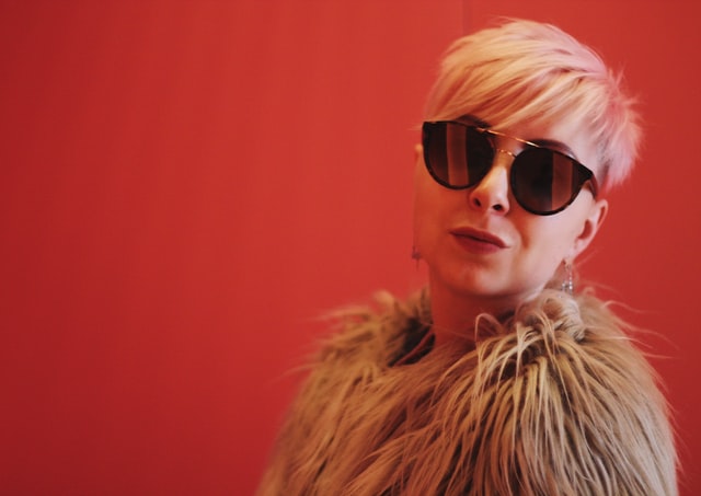 A blond woman wearing reflective sunglasses against a red background.