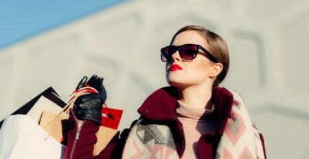 A woman in sunglasses holds shopping bags in bright sunshine.