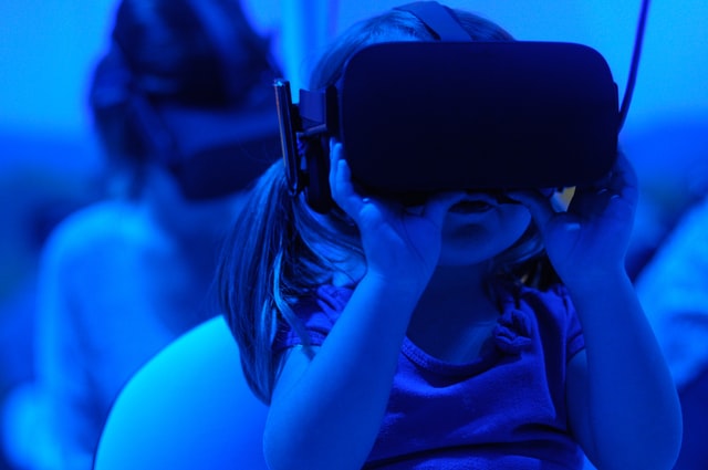 A small child holding virtual reality goggles up to their face in a dark room.