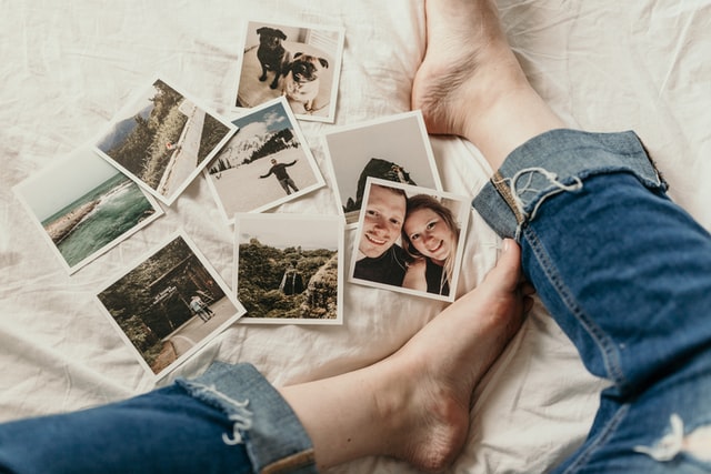 Alt-Text: Some photographs lay scattered on a bed near a leg.