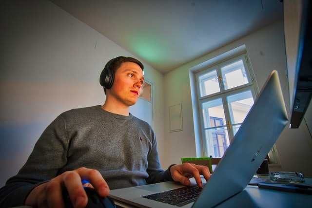 A man wearing headphones works at a computer with two monitors.