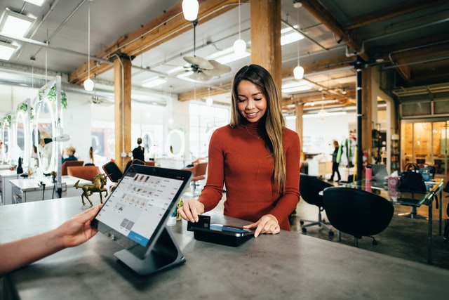 A woman in a red shirt works at a touchscreen cash register.