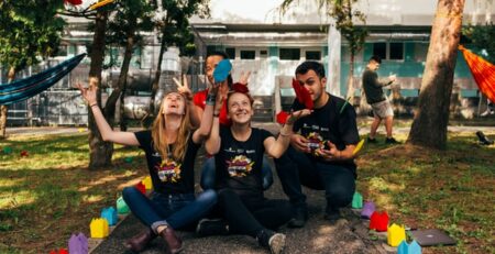 Four people in black shirts throw colorful paper in the air.