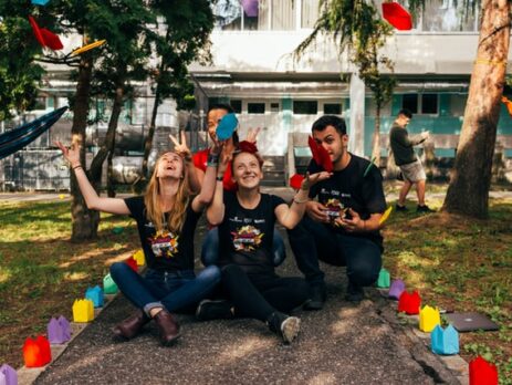 Four people in black shirts throw colorful paper in the air.