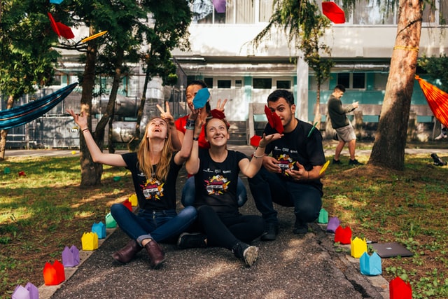 Four people in black shirts throw colorful paper in the air.