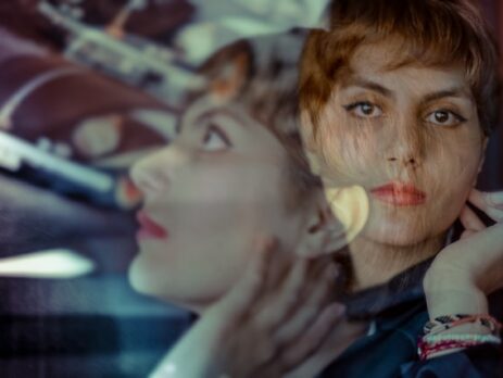 A double exposure of a woman with short hair in a turquoise shirt.