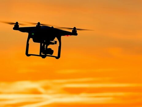 A man controlling a robot is silhouetted by the setting sun.