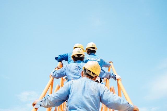 Tree people in hard hats and goggles inspect factory machinery.